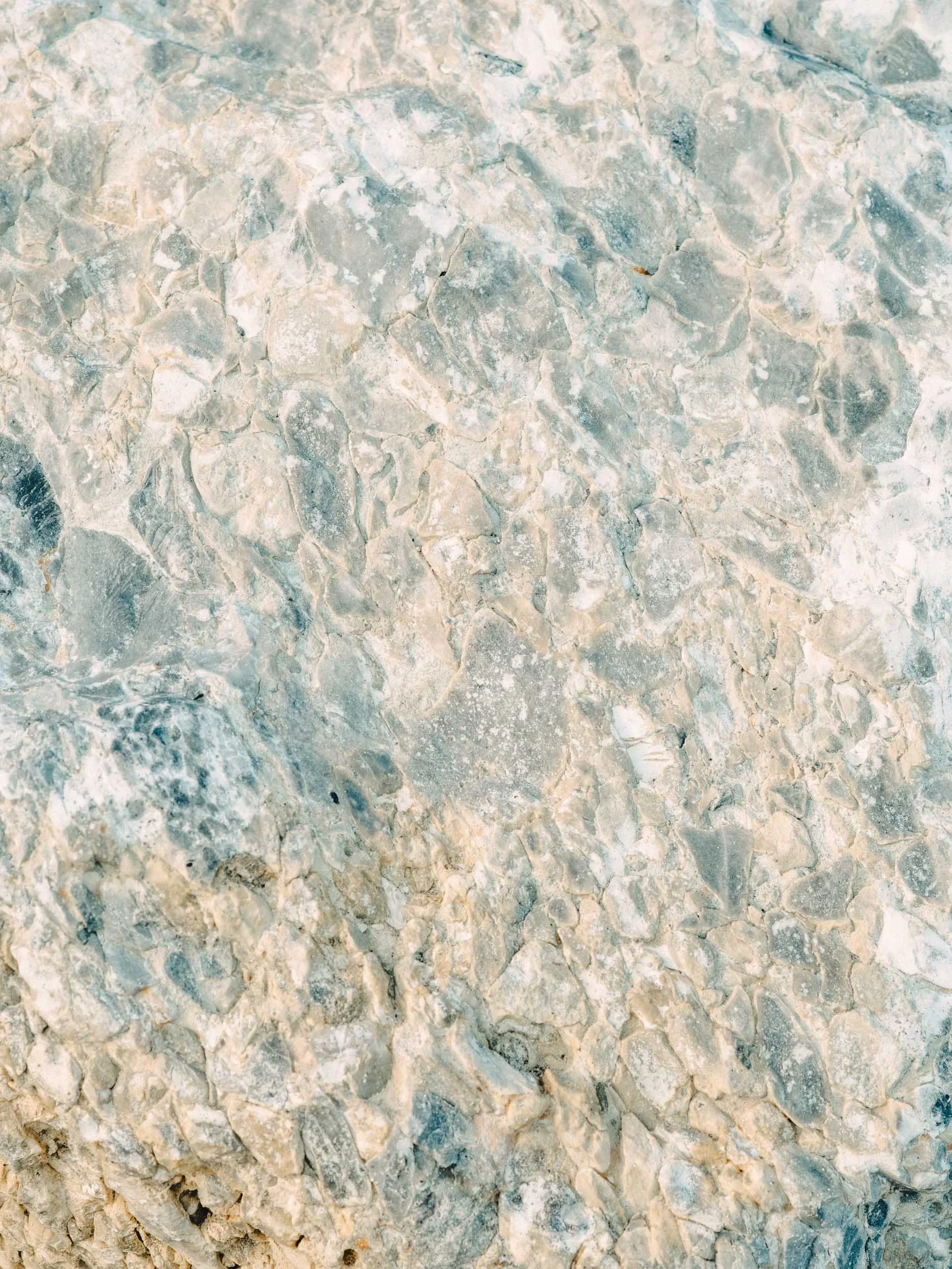 Close-up of a textured, natural stone surface with varying shades of beige, gray, and white.