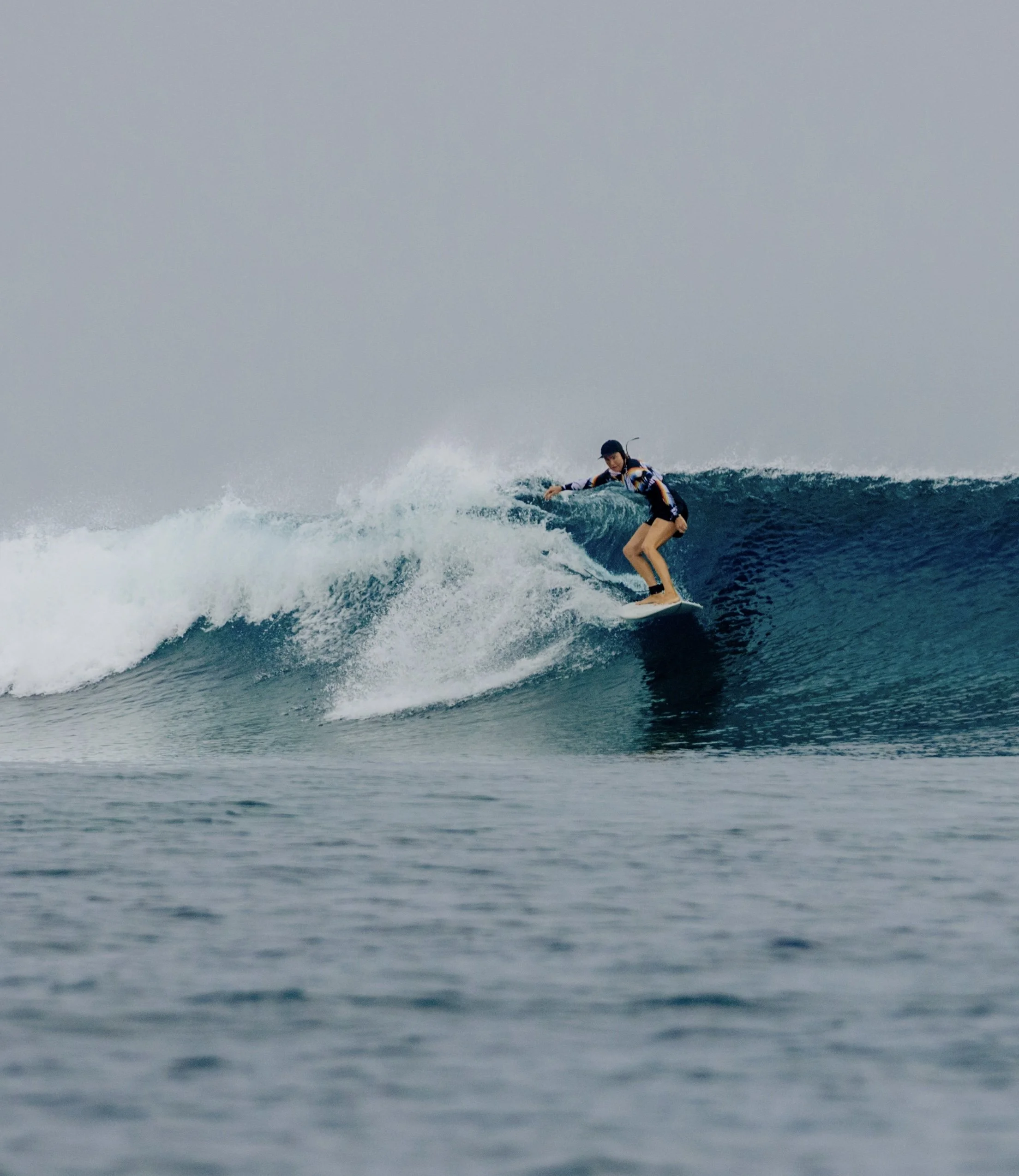 Person surfing on a wave in the ocean under a cloudy sky.