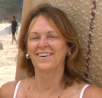 A woman smiling and leaning against a palm tree at the beach.