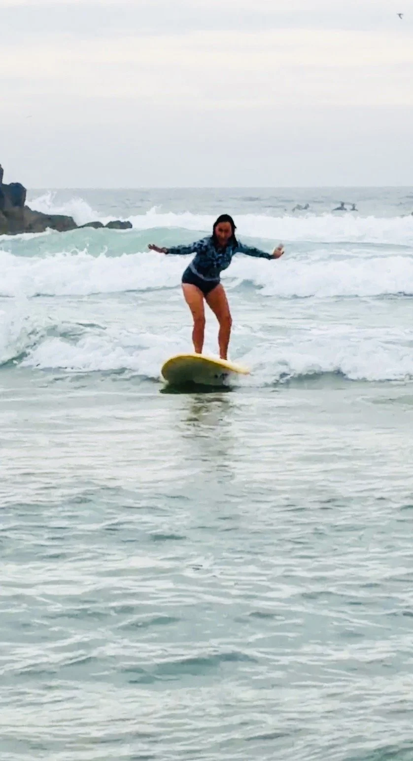 Woman surfing on a yellow surfboard in the ocean during overcast weather.