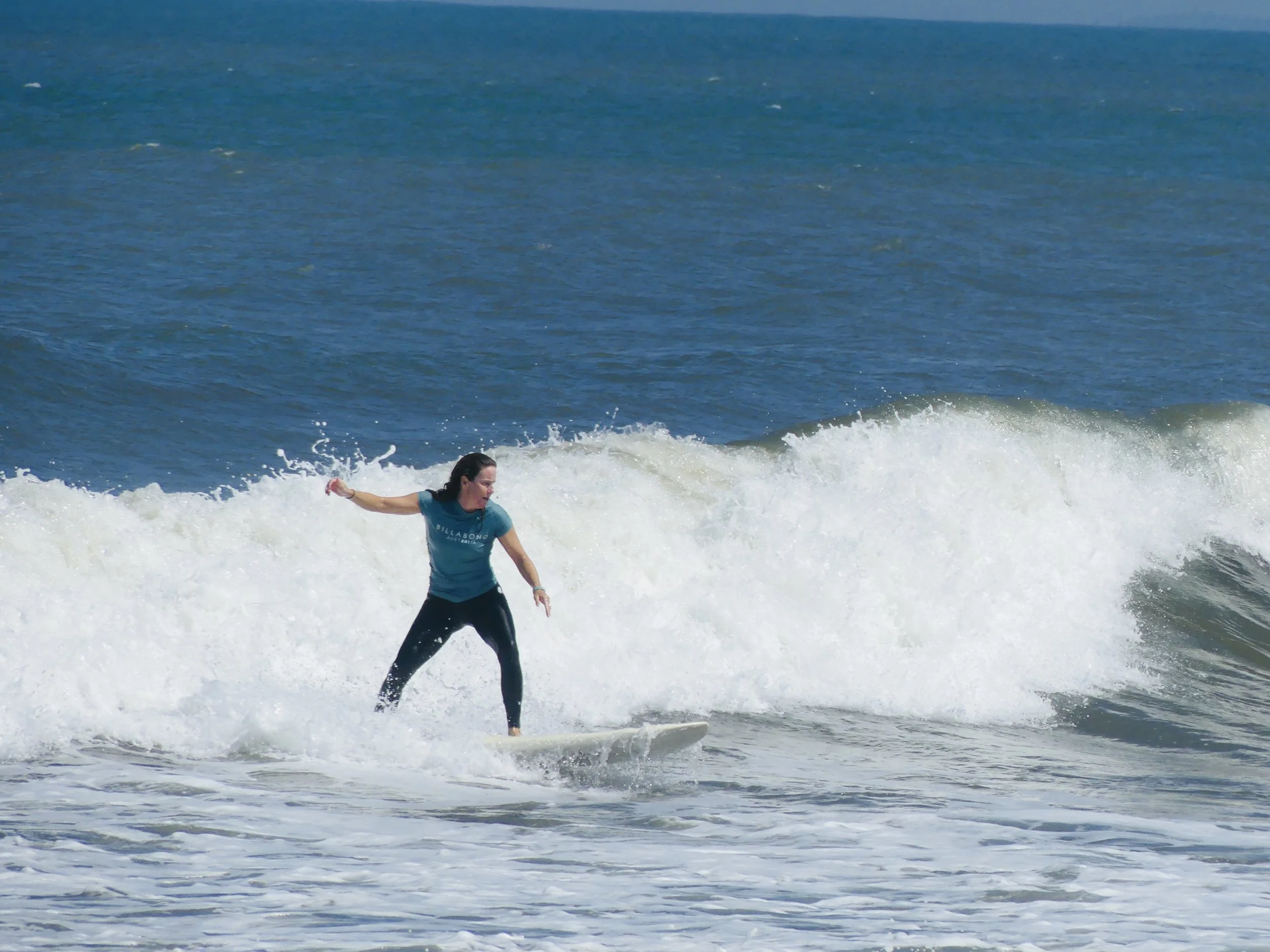 A woman surfing on a wave in the ocean with a clear blue sky.
