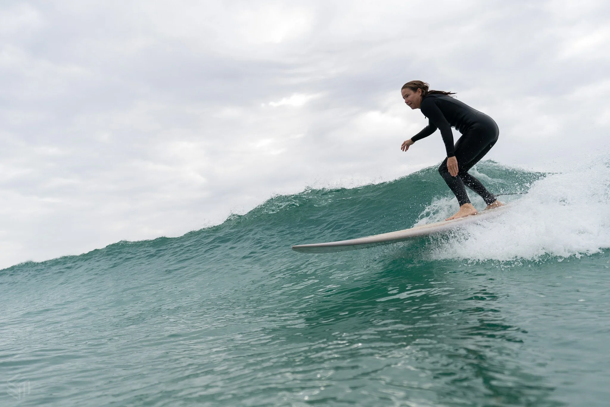 Woman in a black wetsuit surfing on a small wave during cloudy weather.