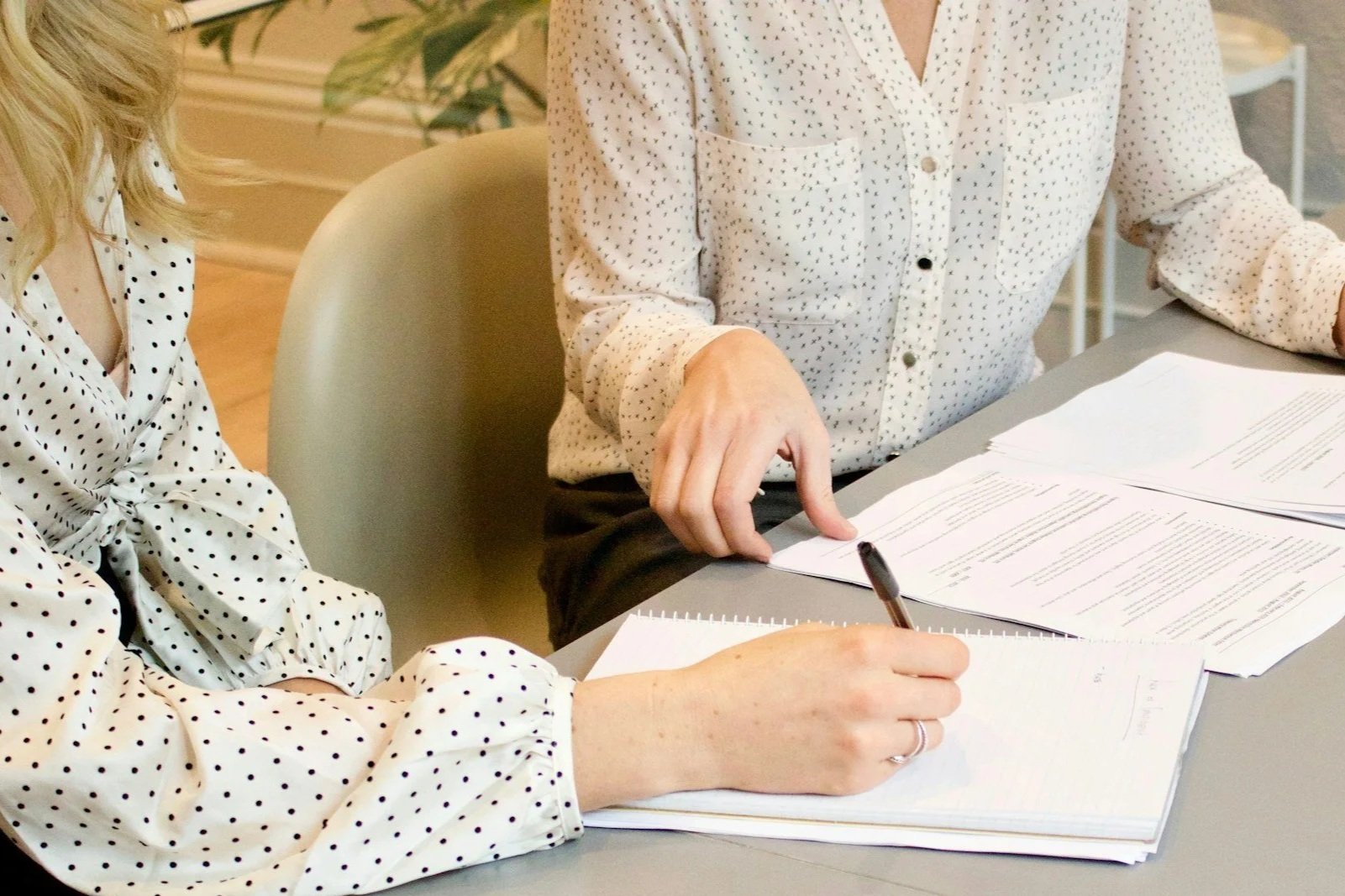 Two people in polka dot shirts sitting at a desk with papers and notebooks, one person is writing with a pen.