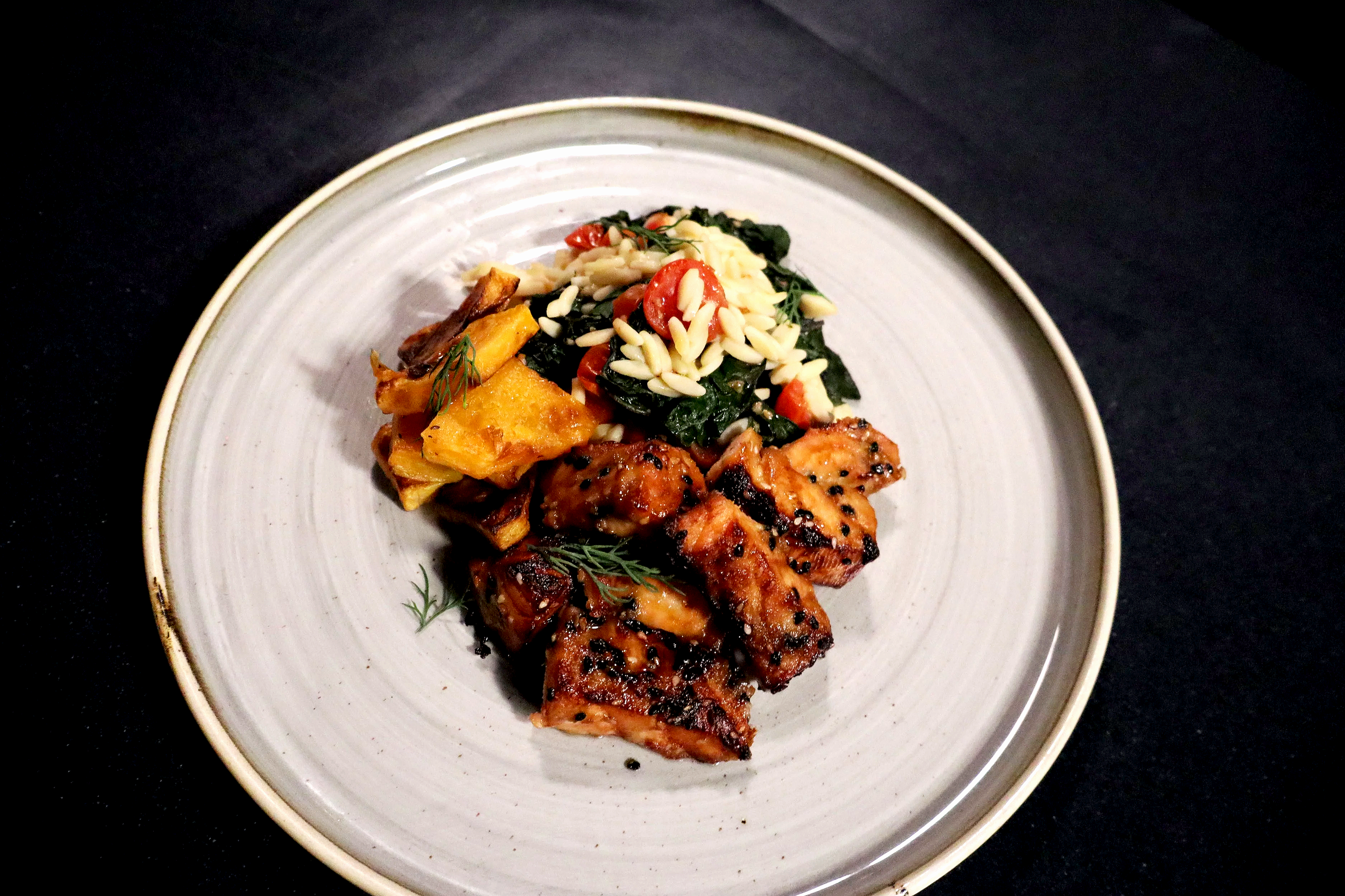 A white ceramic plate with grilled chicken, a mixed vegetable salad with torn greens, cherry tomatoes, slivered almonds, and shredded cheese, and roasted sweet potatoes garnished with sprigs of dill.