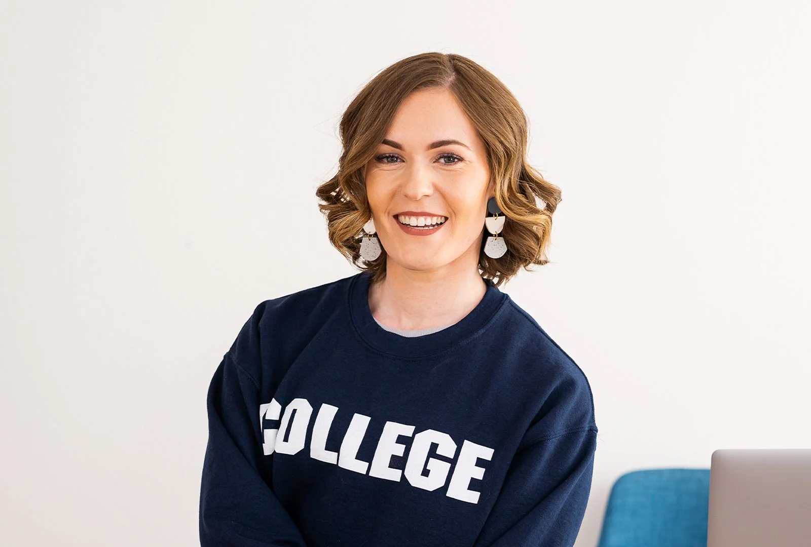 Carly Gieszl smiles at the camera while wearing a blue sweater reading college