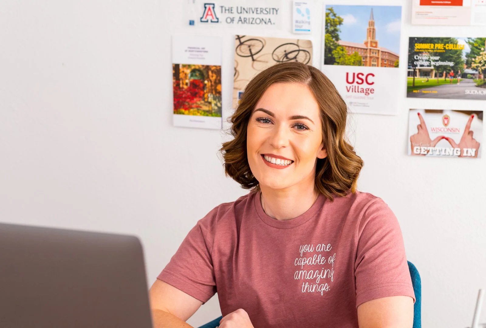 Carly Gieszl smiles at the camera while sitting at her desk wearing a pink shirt