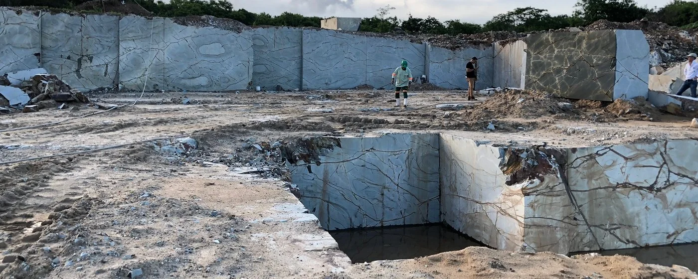 Workers inspecting a large marble quarry with cut marble blocks and a deep cut into the earth.