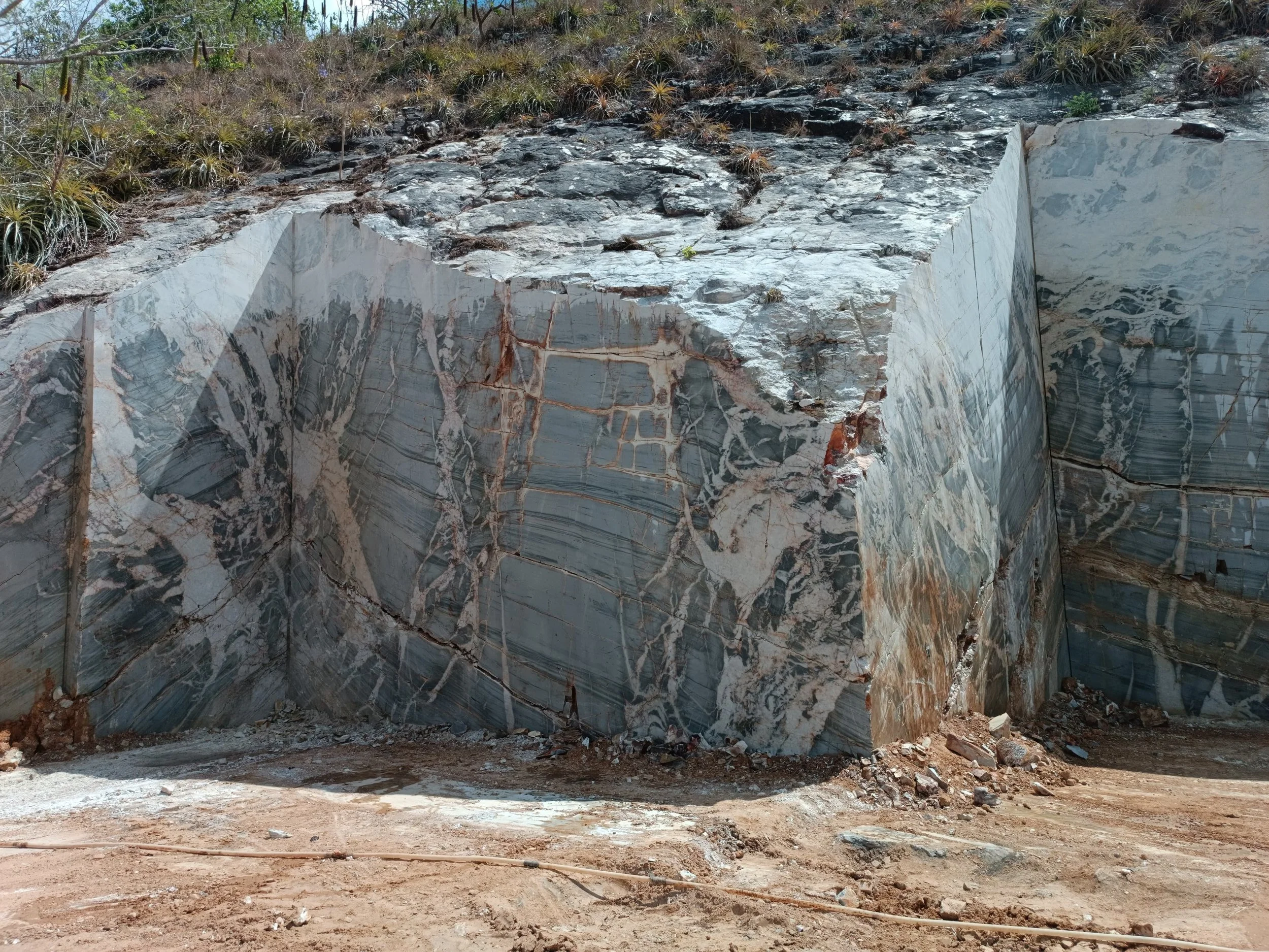 A large marble quarry with cut marble blocks and a dirt ground, surrounded by trees and shrubbery.