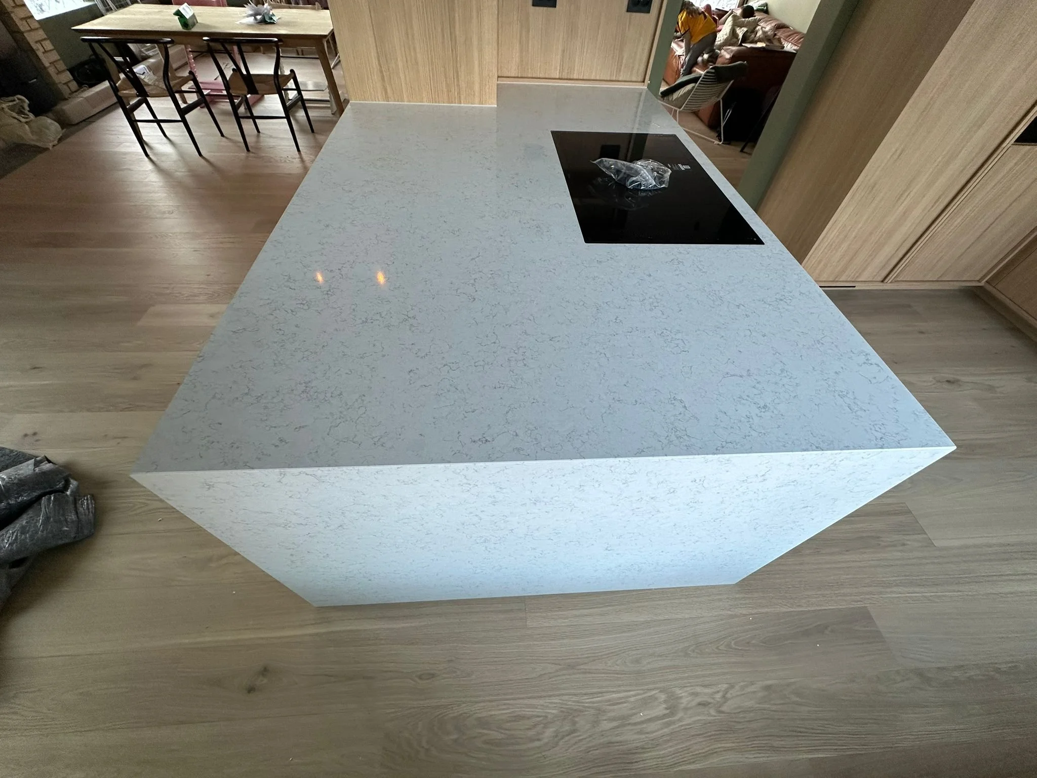 A modern kitchen island with a speckled gray countertop and black cooktop, situated in a kitchen with wooden cabinets and a light wooden floor.