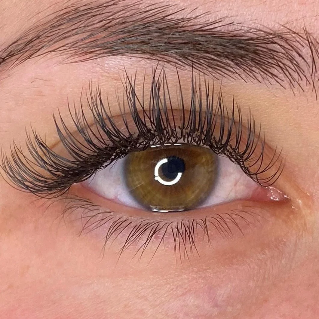 Close-up of a human eye with brown iris, long eyelashes, and well-groomed eyebrow.
