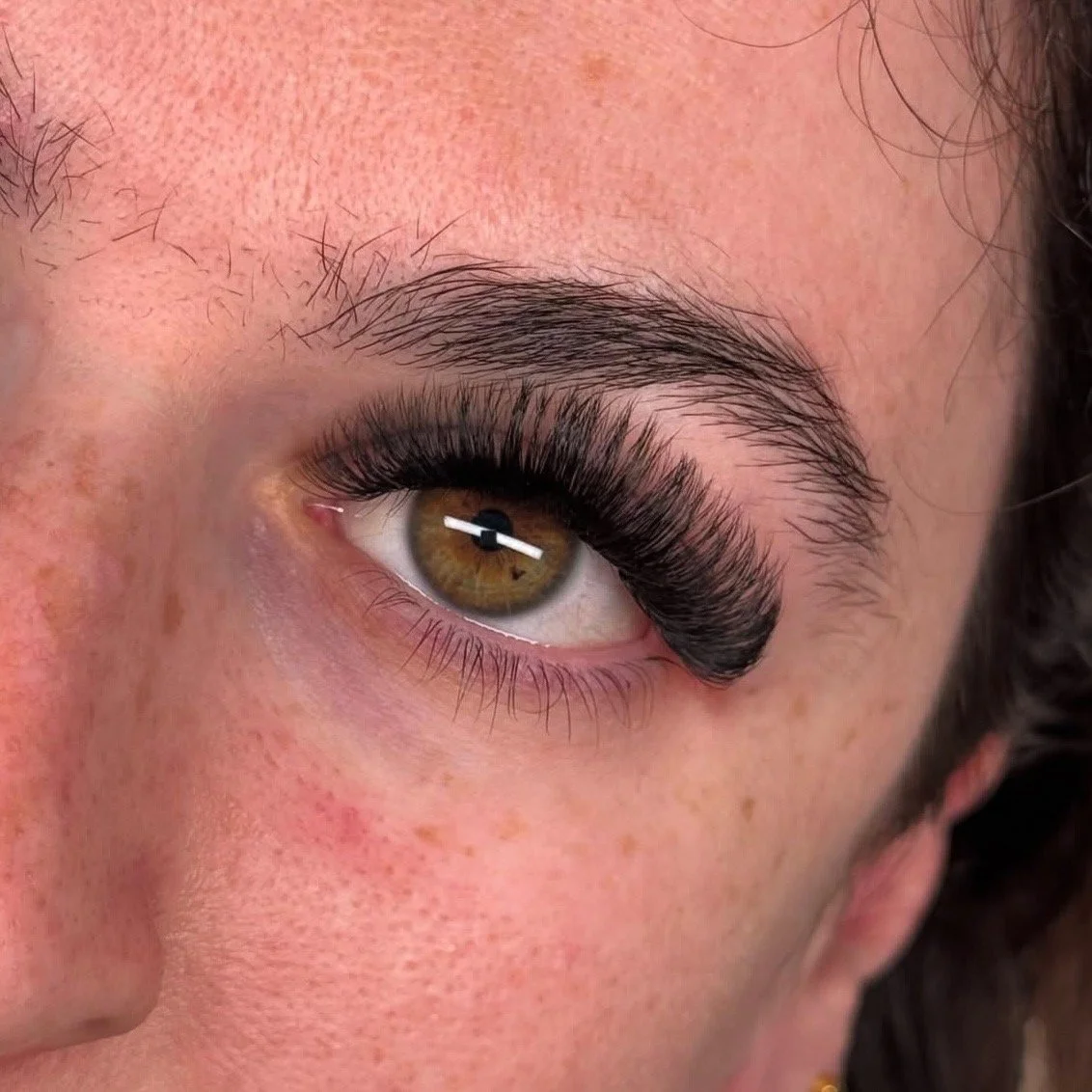 Close-up of a woman's face, focusing on her hazel eye with long eyelashes and well-groomed eyebrow.