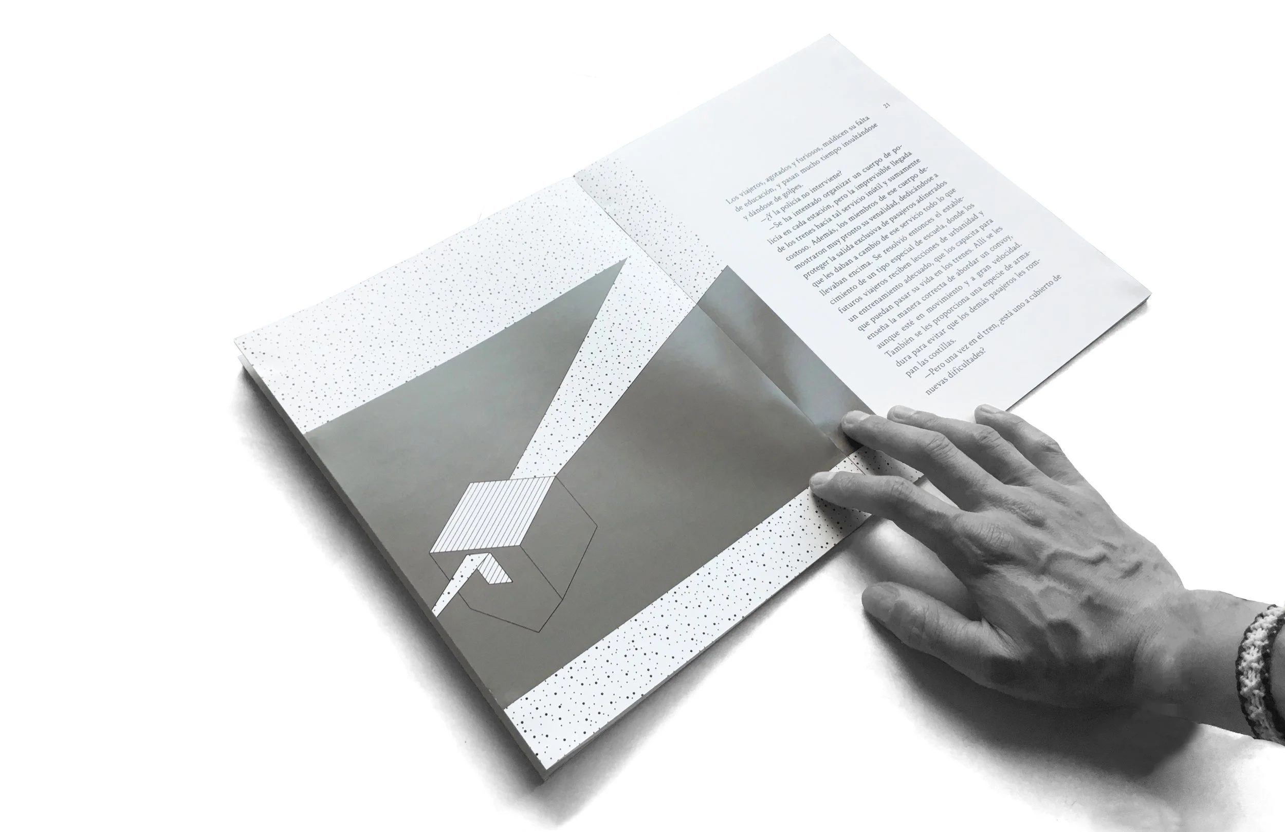 A person's hand turning a page of an open booklet with geometric and dotted design on the left page and text on the right page.