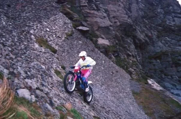 A person riding a motorcycle on a steep rocky path on a mountain trail.