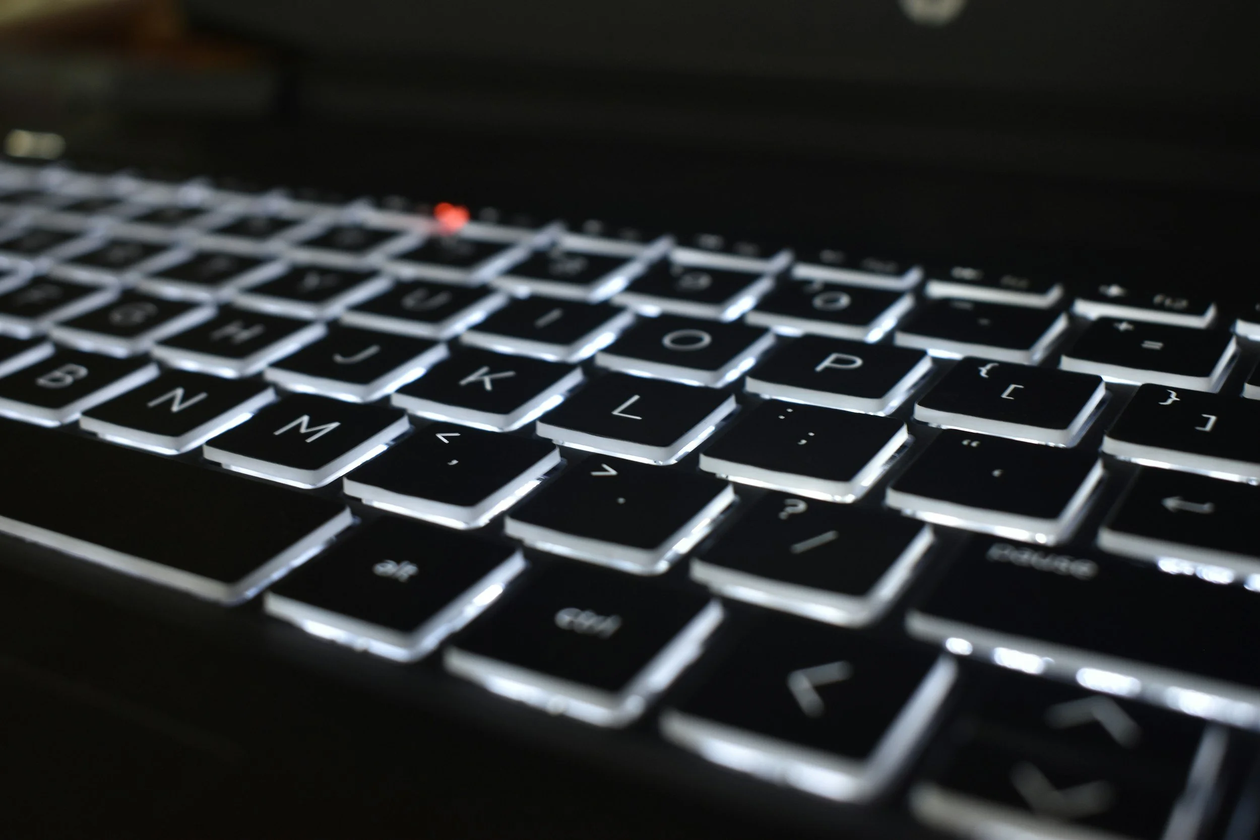 Close-up of a black keyboard with illuminated keys in a dimly lit environment.
