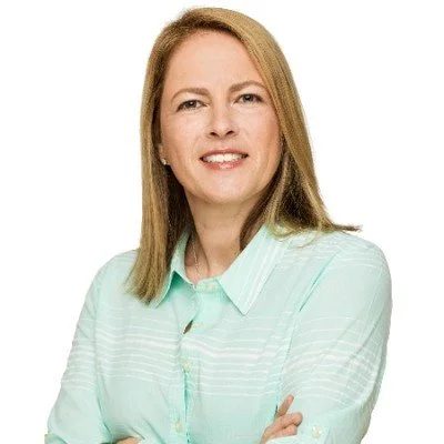 A woman with shoulder-length blonde hair, wearing a light green button-up shirt, smiling with arms crossed against a plain white background.