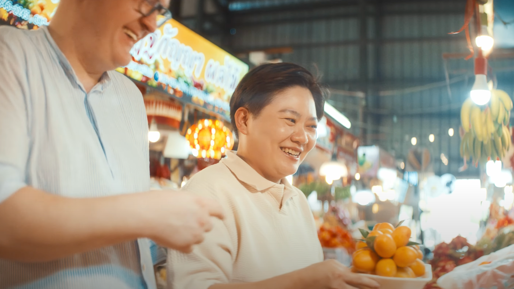 A woman smiling while holding a plate of yellow-orange fruit at a market.