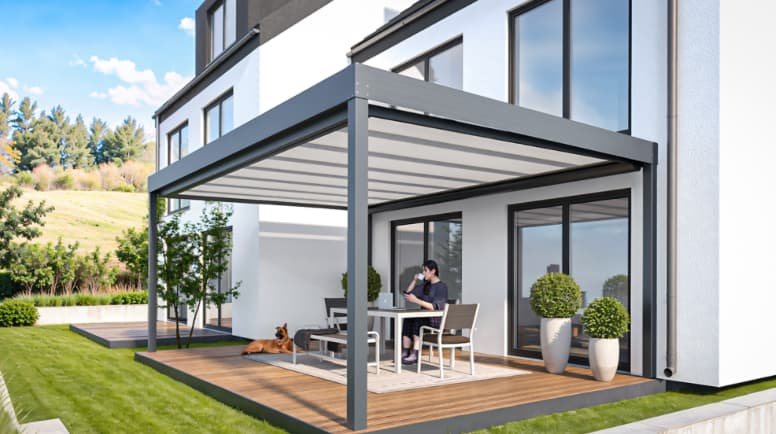 Man zit aan tafel op patio met planten en hond in tuin, modern huis op achtergrond