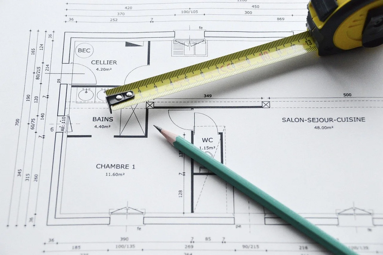 Architectural blueprint of an apartment layout with a measuring tape and a pen placed over it, showing various rooms like a bedroom, bathroom, and living area.