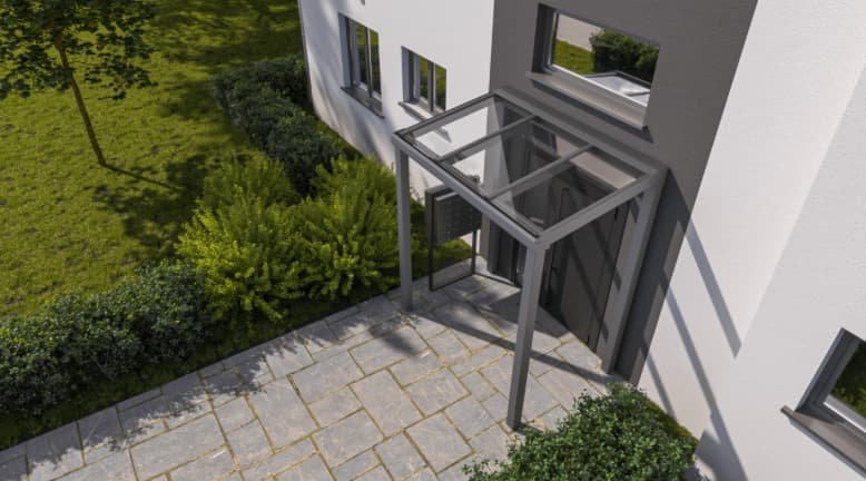 Moderne woning met een glazen overkapping boven de ingang, omgeven door een betegeld terras en groene struiken.
