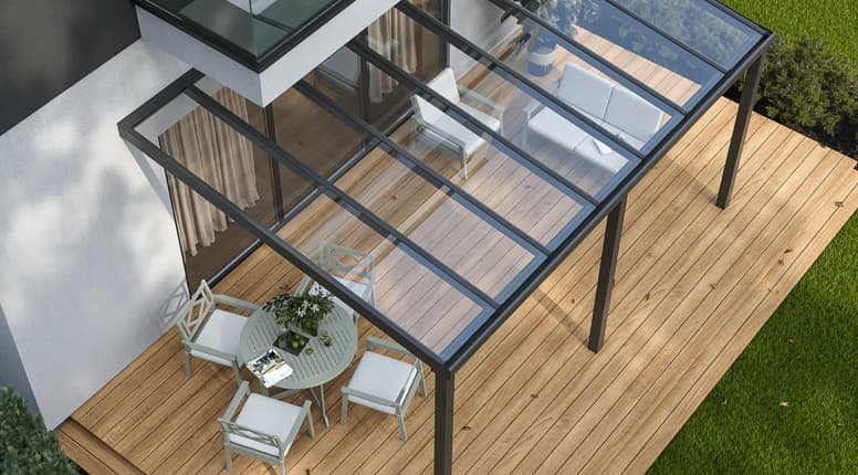 Buiten terras met houten vloer en een glazen afdak, met een ronde tafel, vier stoelen en een plant erop.