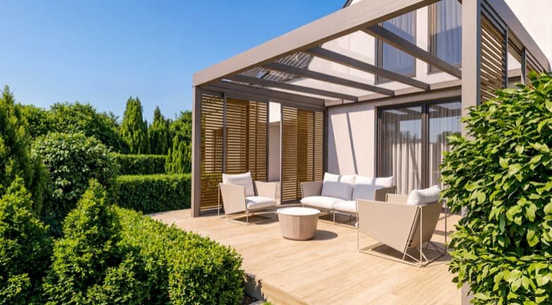 Terras met tuinmeubilair voor een modern huis met grote ramen en overkapping, omgeven door groene struiken