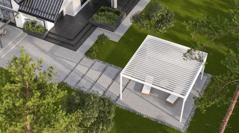 Een vogelperspectief van een tuin met moderne tuinmeubelen onder een pergola, nabij een woning, omgeven door groene gras en bomen.