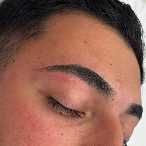 Close-up of a person's closed eye, showing well-groomed eyebrows and clear skin.