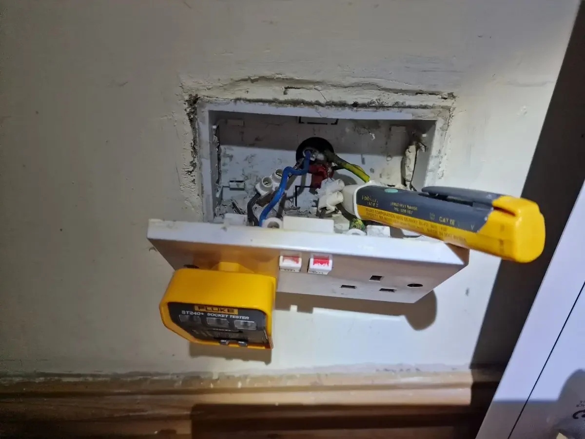 Electrical work in progress with a socket tester and electrical tester on an open wall socket.