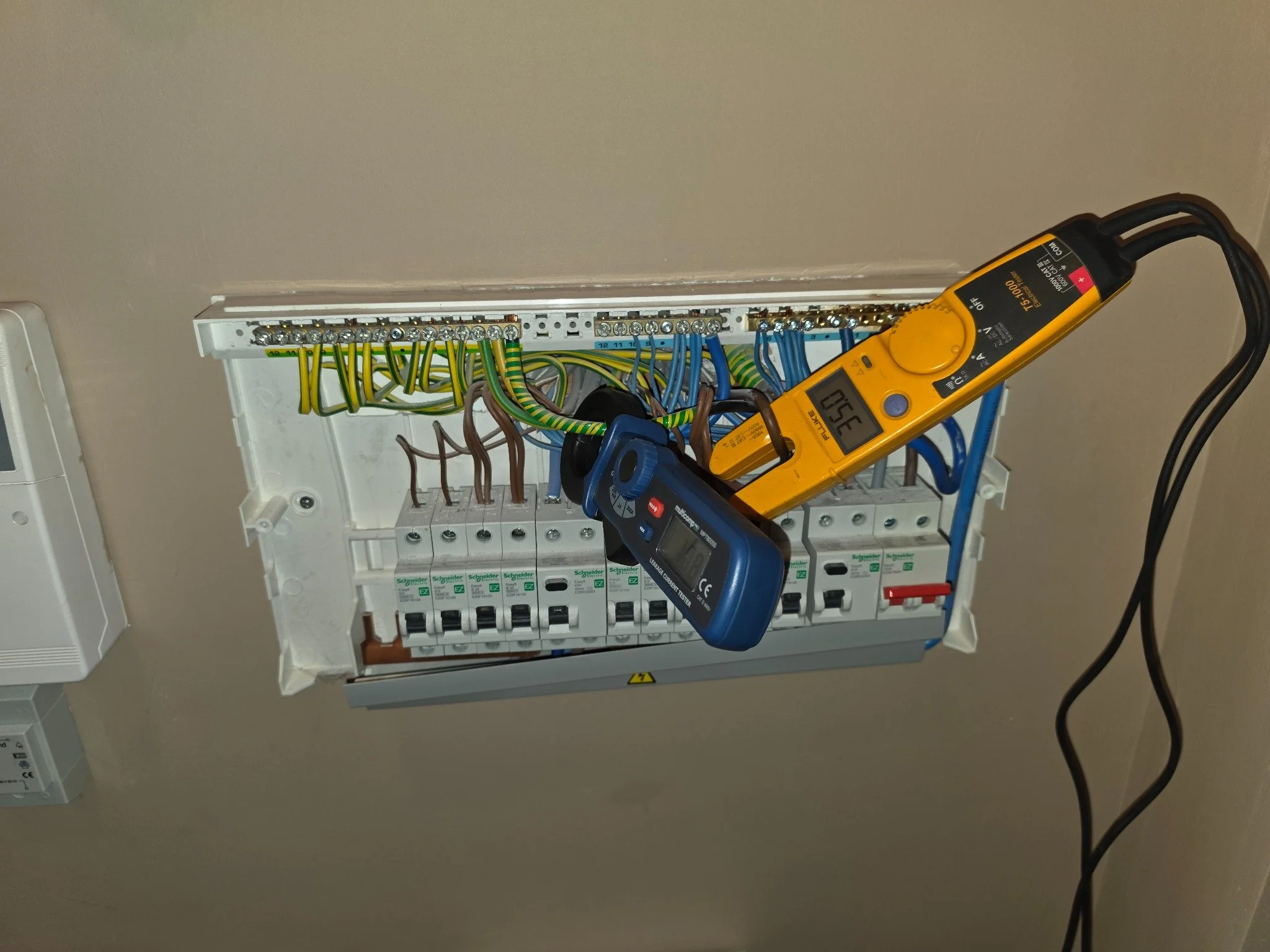 5. Load-check stage: the open consumer unit with electrical test instruments in use.