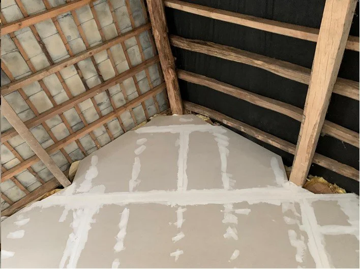 Interior view of an attic with unfinished walls and roof, showing wooden beams and a partially completed wall with insulation and drywall.