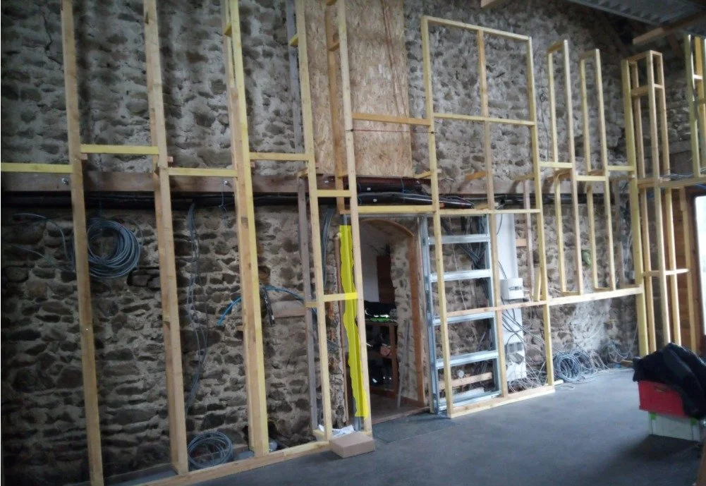 Interior view of a building under construction with exposed stone walls and wooden framing for a wall or door opening.