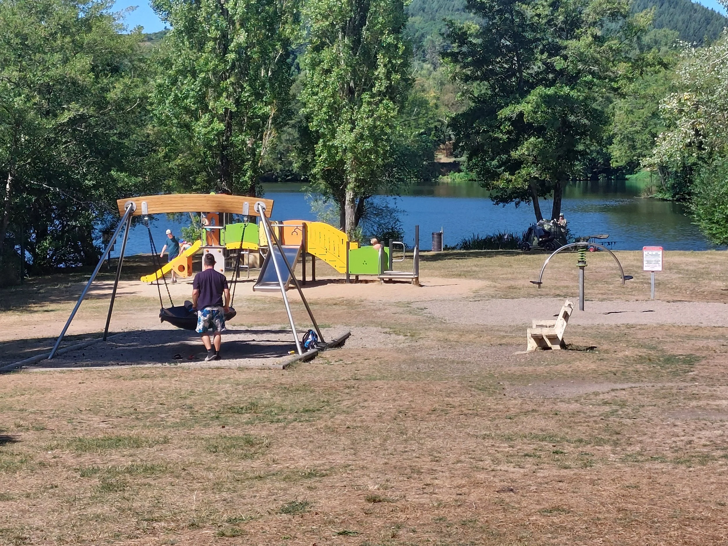 Kids playing on a playground near a lake with trees and hills in the background.