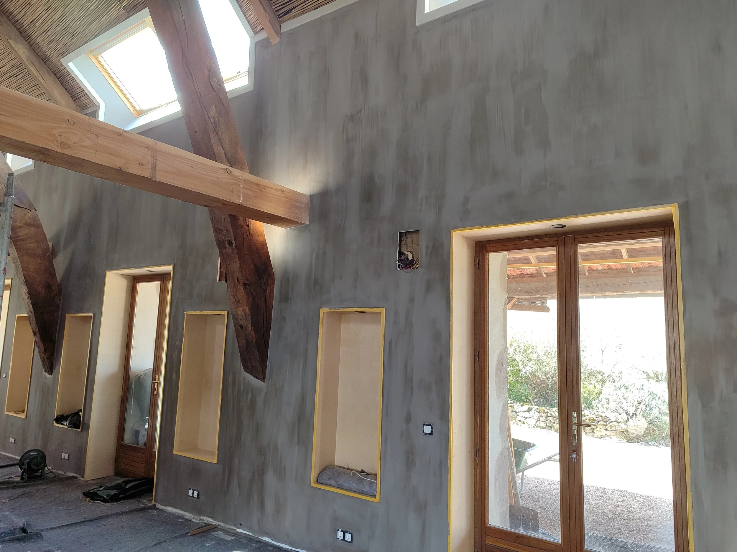 Interior of a house under construction with unfinished walls, exposed wooden beams, and large windows.