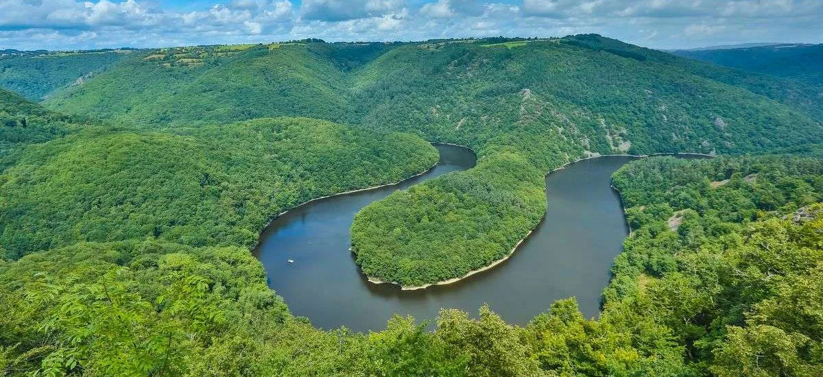 A winding river surrounded by lush green forests and rolling hills under a partly cloudy sky.