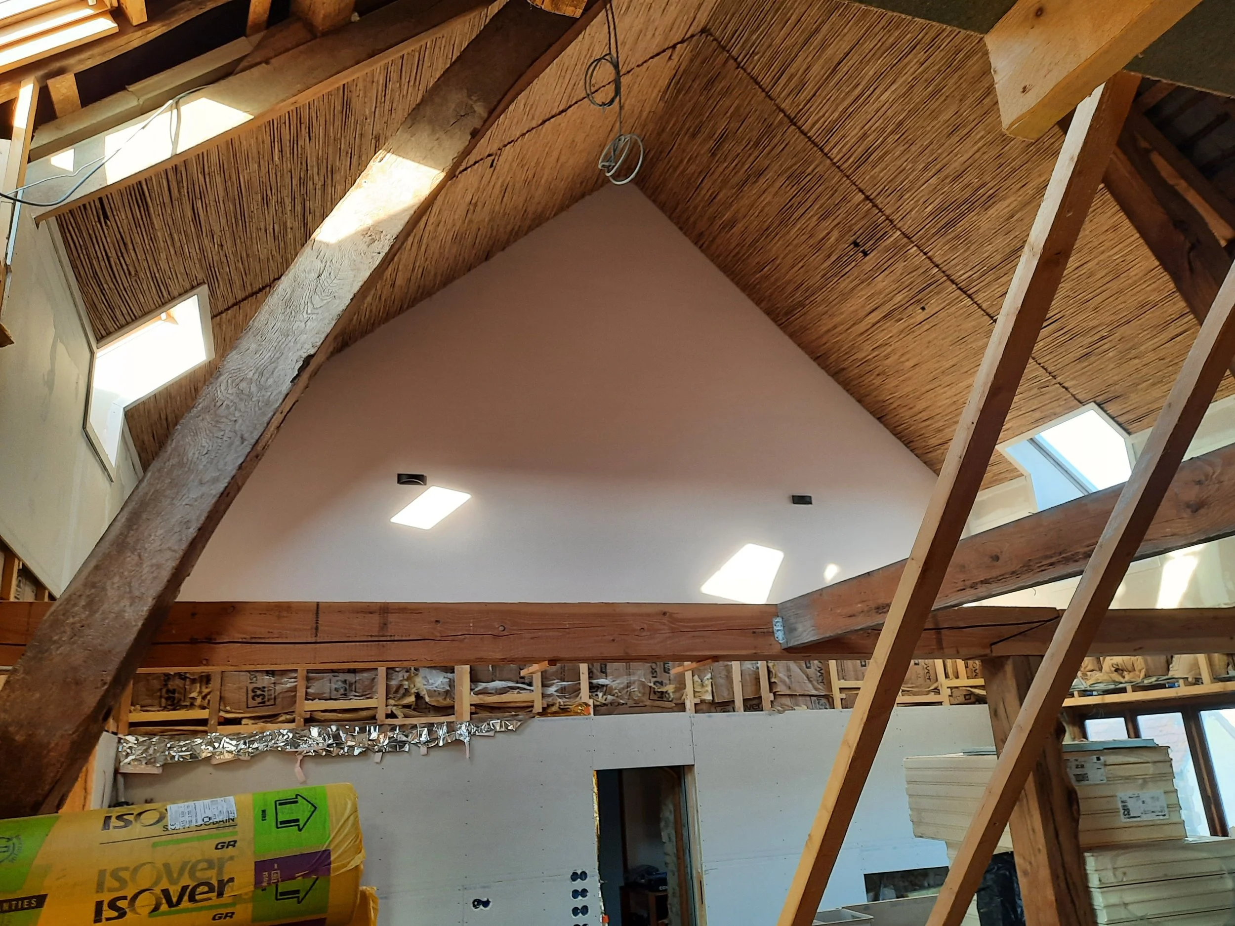 Interior of a building under construction with exposed wooden beams, insulation material, and temporary lighting.