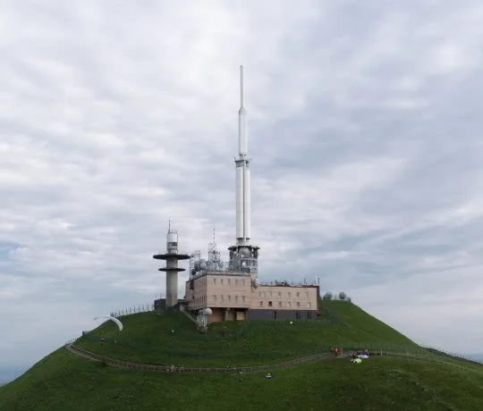 Radio and communication towers on a hilltop with a cloudy sky in the background.