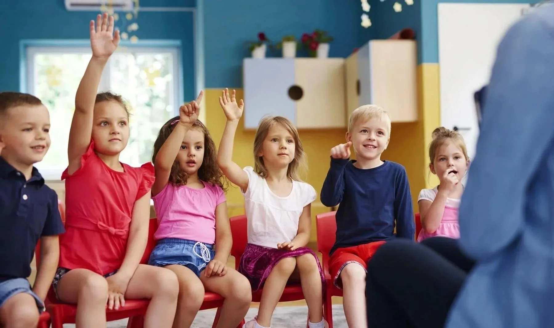 Young children raising their hands during a speech and language activity