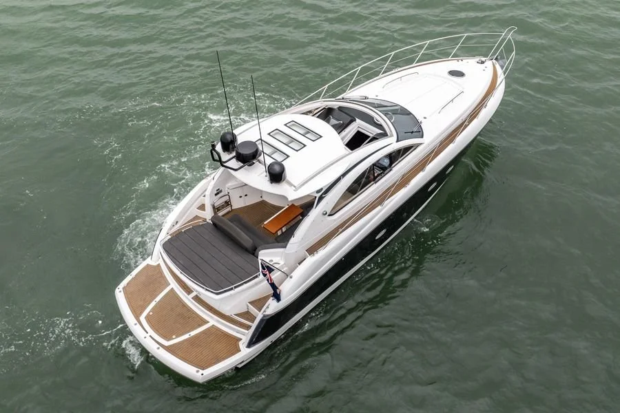 A white luxury motor yacht with wood accents sailing on green water, showing the deck, cockpit, and bow.