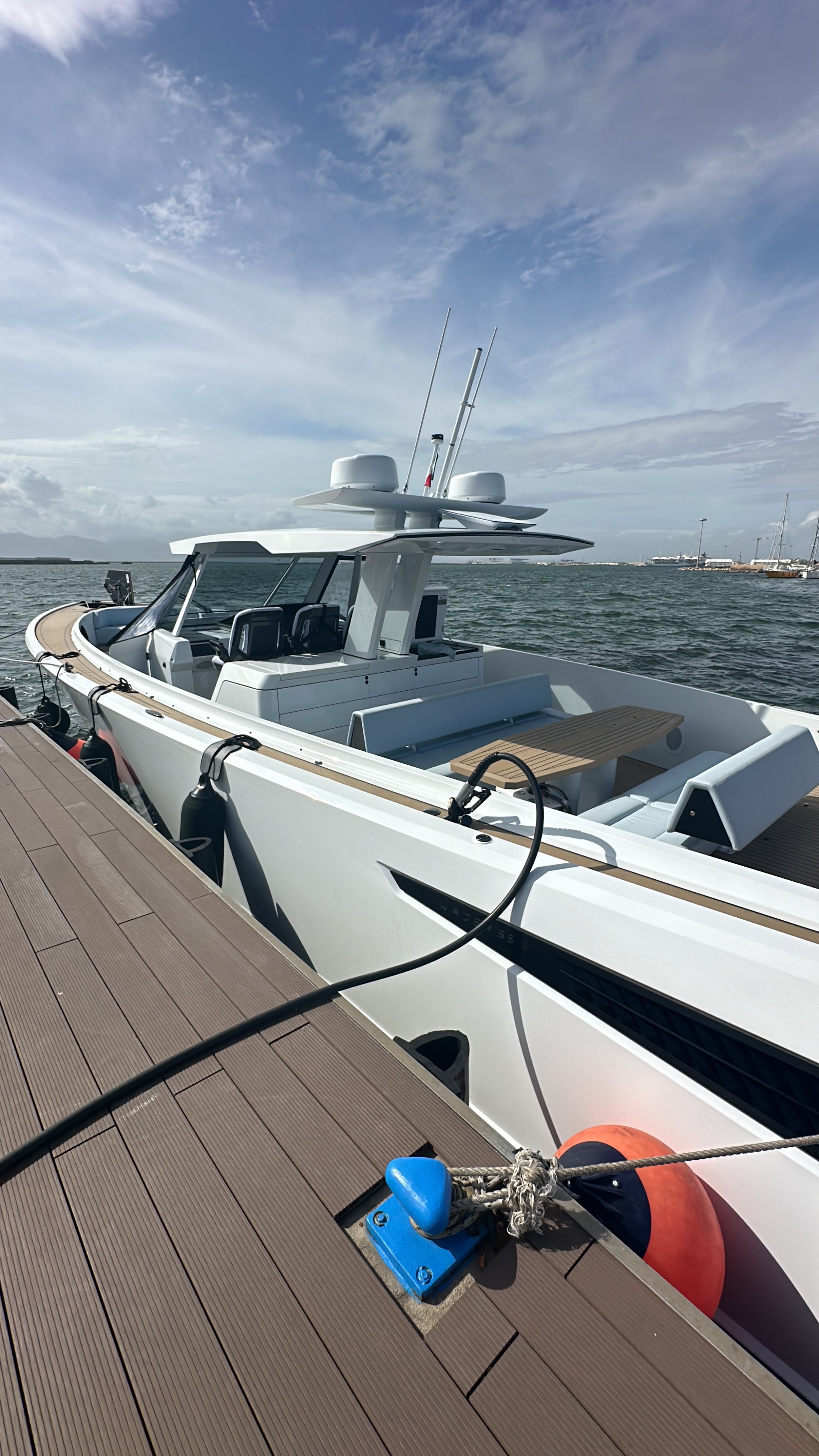 White yacht docked at a wooden pier with a calm water body and a cloudy sky in the background.