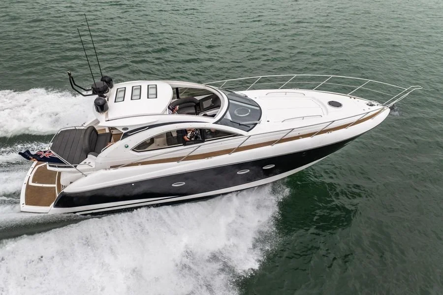 A white and black luxury motorboat cruising on the water with a wooden deck at the stern and a small flag at the back.