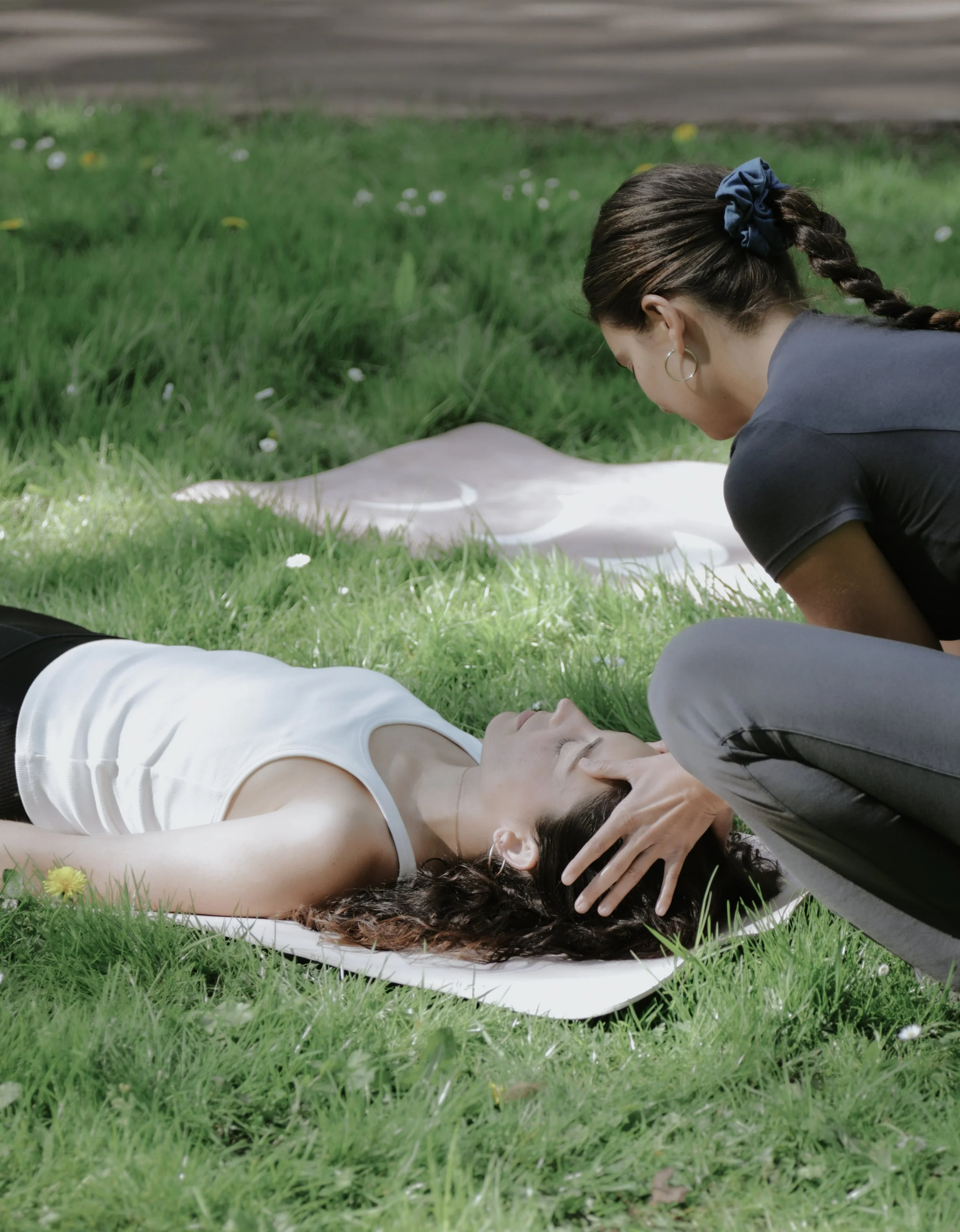 Sesión de terapia corporal al aire libre, con una terapeuta acompañando a una persona tumbada sobre la hierba.
