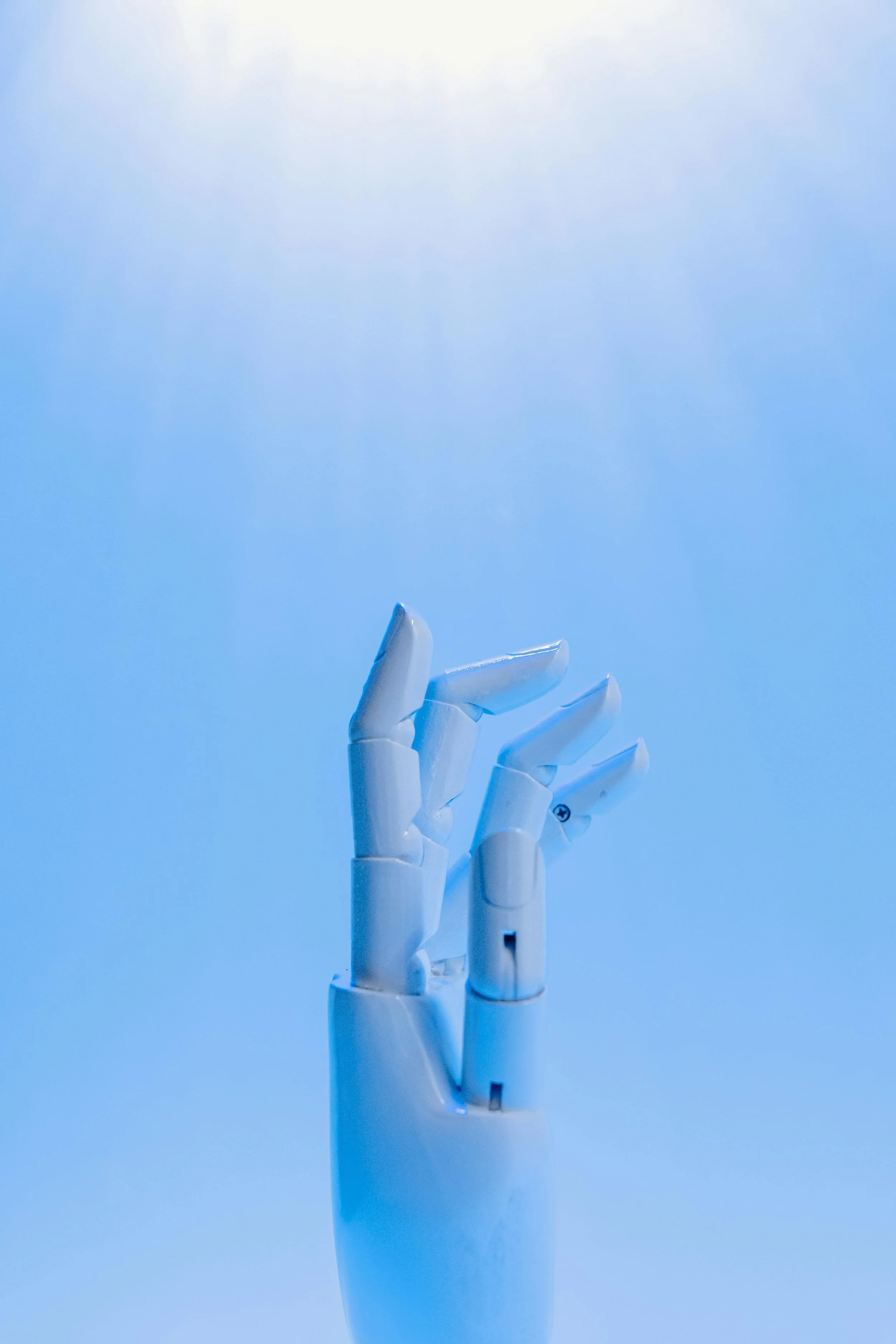 Close-up of a white robotic hand raised against a gradient blue background.
