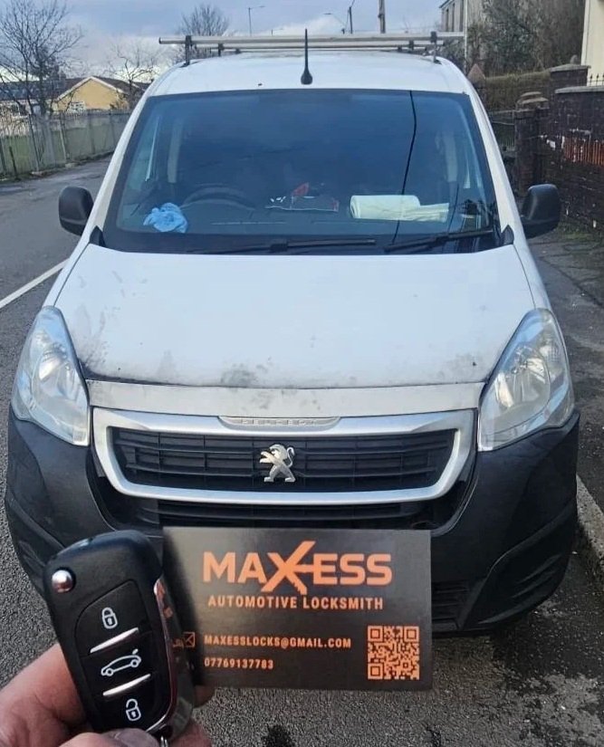 A white Peugeot van parked on a street, with a business card for Maxess Automotive Locksmith held in front of the camera, including contact information and a key fob.