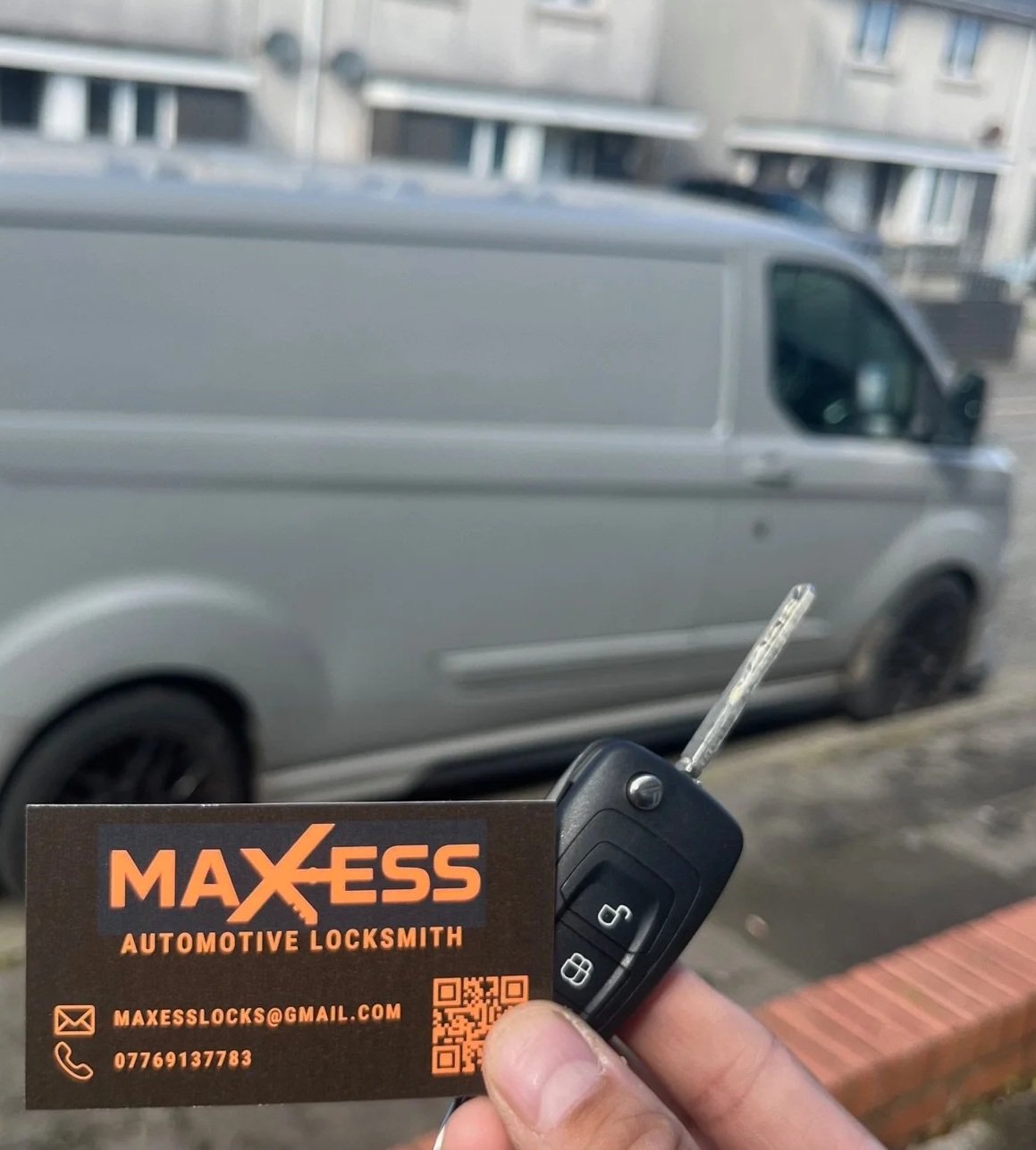 Hand holding a car key and a business card for Maxess Automotive Locksmith with a blurred silver van in the background.