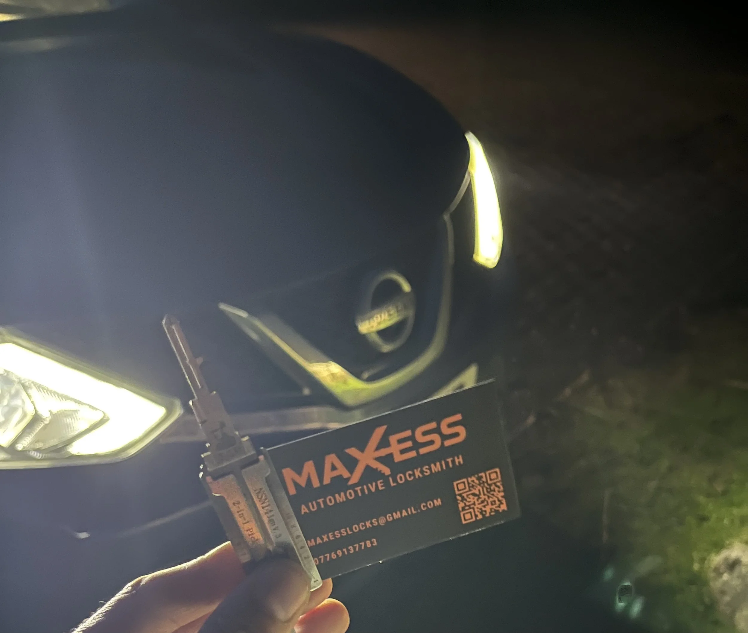 Close-up of a black Mercedes-Benz car with a MAXxESS auto locksmith business card and a key in the foreground, taken at night.
