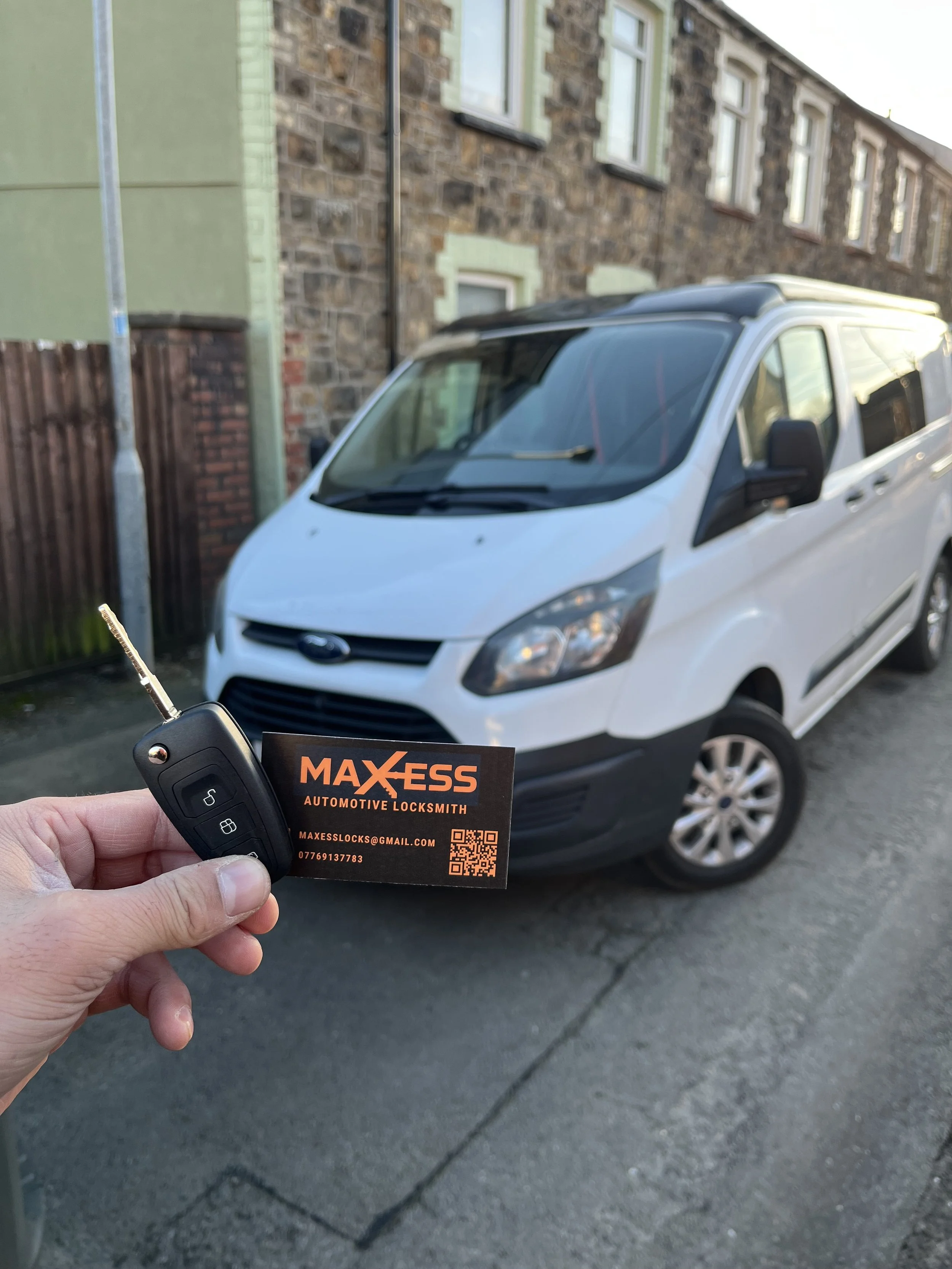 A person holding a car key and business card in front of a white Ford Transit van parked on the street.
