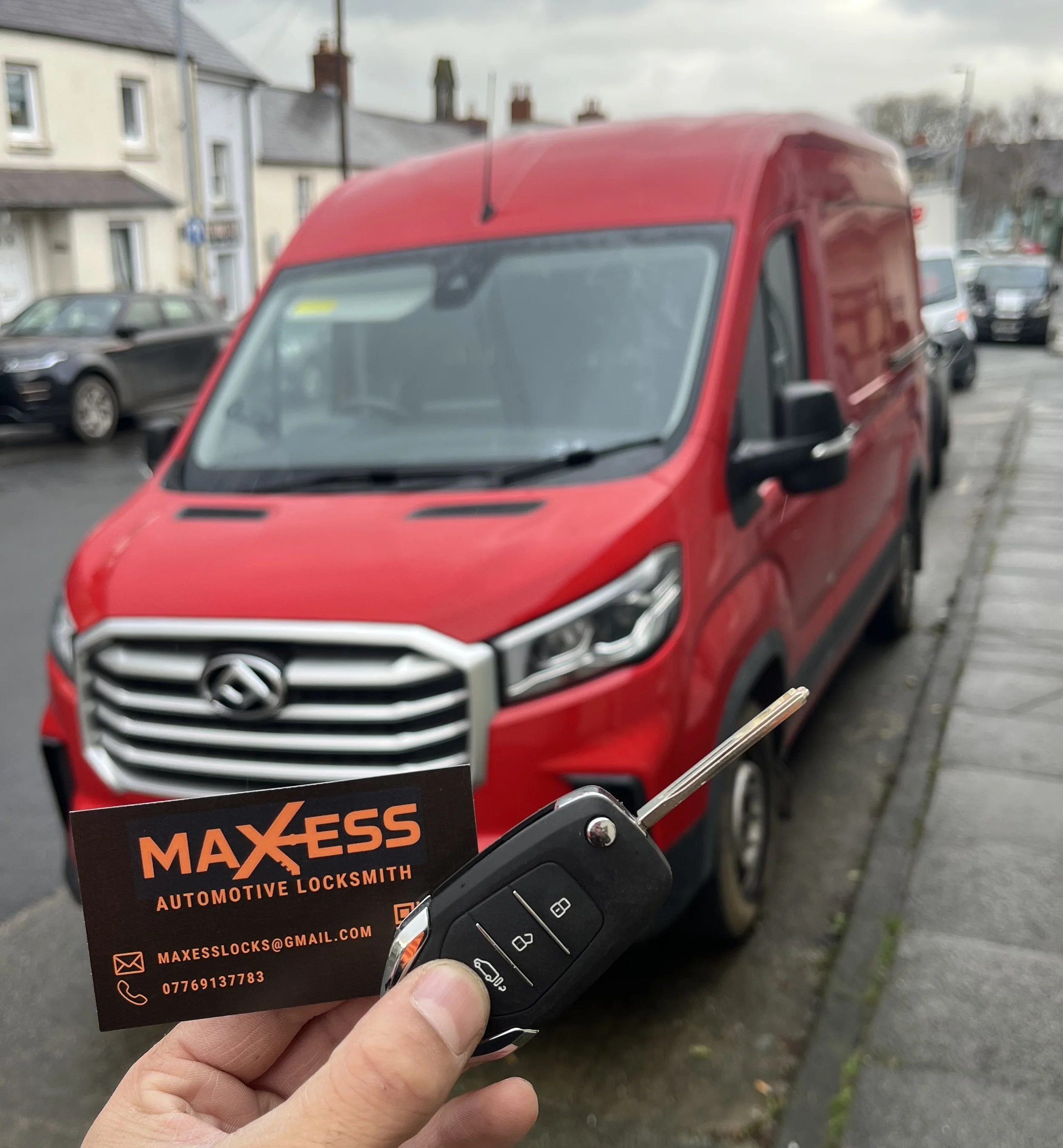 A person holding car keys and a business card in front of a red van parked on a street.