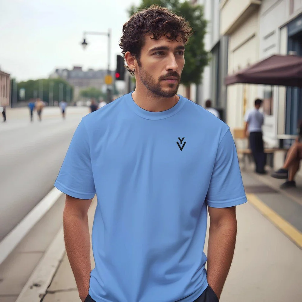 A man in a light blue T-shirt standing on a city sidewalk.
