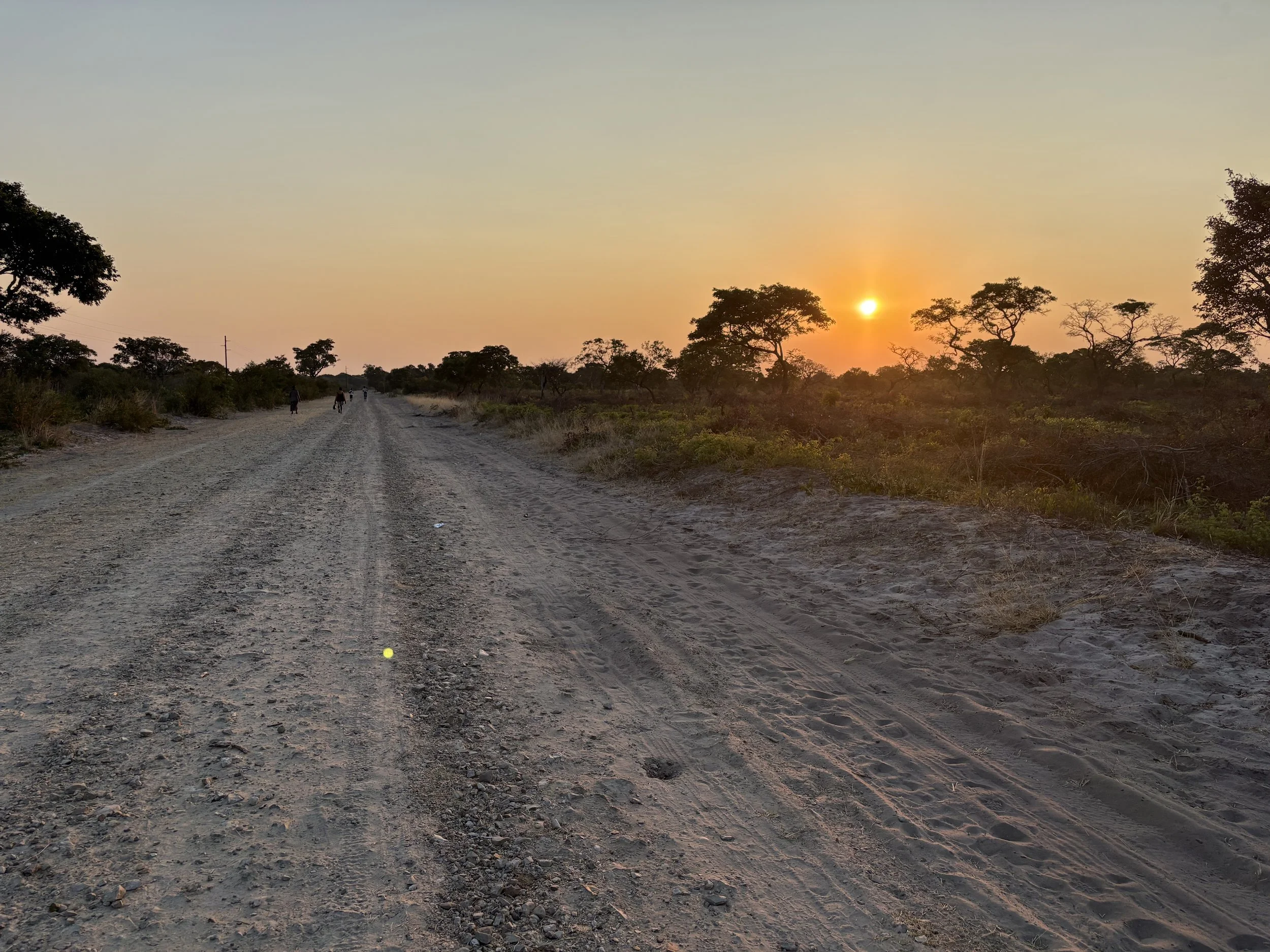 People walking along a gravel road at sunset in Africa