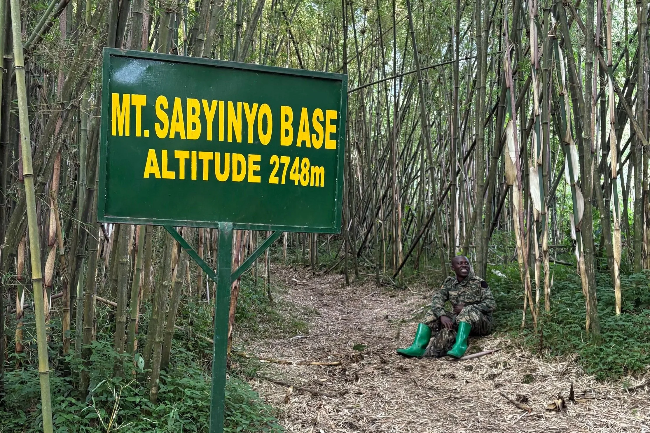 A park ranger sits beside the Mount Sabyinyo base marker at the trailhead in Mgahinga National Park, Uganda.